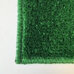 Close-up of the corner of a rectangular Graveside Grass mat in green, displayed on a white surface.