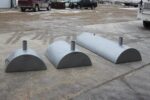 Three gray metal Frost Removers, resembling semi-cylindrical structures with small vertical pipes on top, are placed on a concrete surface outdoors, with parked vehicles in the background.