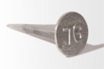 A product from the Cast Aluminum Lot Markers range, showcasing a metal spike with the number 76 embossed on its circular head, set against a plain background.