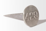 A large nail with a circular head and the number "429" engraved on it, similar to Cast Aluminum Lot Markers, rests on a plain surface.