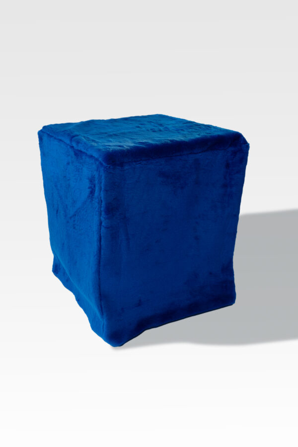 A cube-shaped ottoman with a blue velvet cover elegantly stands against a light gray backdrop, echoing modern sleek designs and adding sophistication similar to the EZ Fold Cremation Stand.