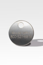 The Cremation ID Disc, a round metal tag, is typically used as a Cremation ID Disc and features the engraving "Holland Supply 800-527-8818," complete with a hole at the top for attachment.