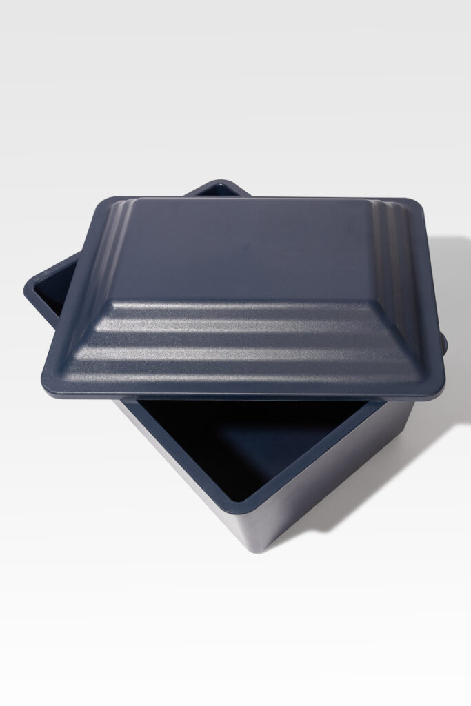 The Safeguard® Urn Vault, a dark gray, square metal container with a matching lid and sturdy design, is depicted open on a light background.