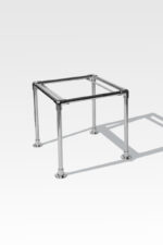 The Stainless Steel Cremation Stand features a sleek design with four cylindrical legs, casting a shadow on a light gray background.