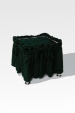 A green, fabric-covered stool with decorative ruffles is set gracefully on a plain background, supported by four metallic feet echoing the design of a Stainless Steel Cremation Stand.