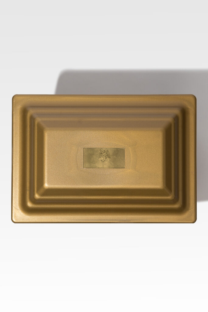 The Fortress® Urn Vault is a rectangular metal container in a gold hue, featuring a small raised emblem at its center, which provides both elegance and durability.