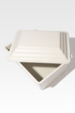 The Safeguard® Urn Vault, featuring a square design with a speckled cream finish and a matching lid, is partially open to reveal its vault-like interior.