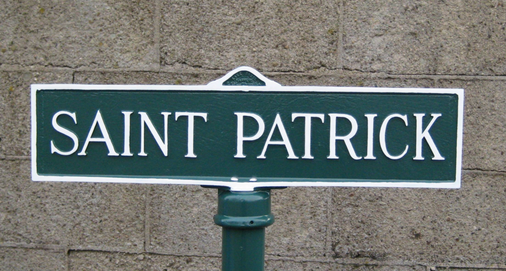 A green street sign with white lettering reads "Saint Patrick" against a gray brick wall, subtly reminding passersby of the top 10 products you must have at your cemetery.