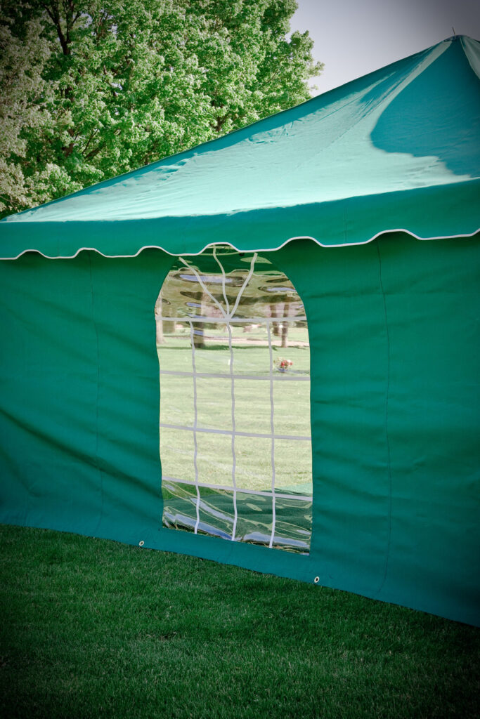 Green event tent with arched window panel set up on a grassy area with trees in the background, reminiscent of the top 10 cemetery products for peaceful and serene gatherings.