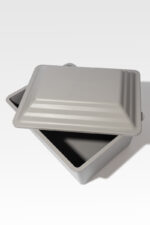 A square metal baking pan with a matching lid is shown, with the lid slightly open.