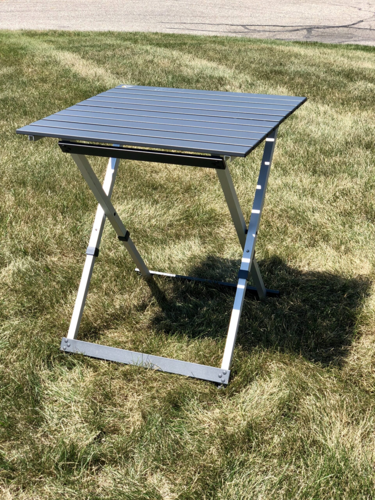 A folding metal table with a slatted surface, often used as cremation stands, is set up on grass outdoors.