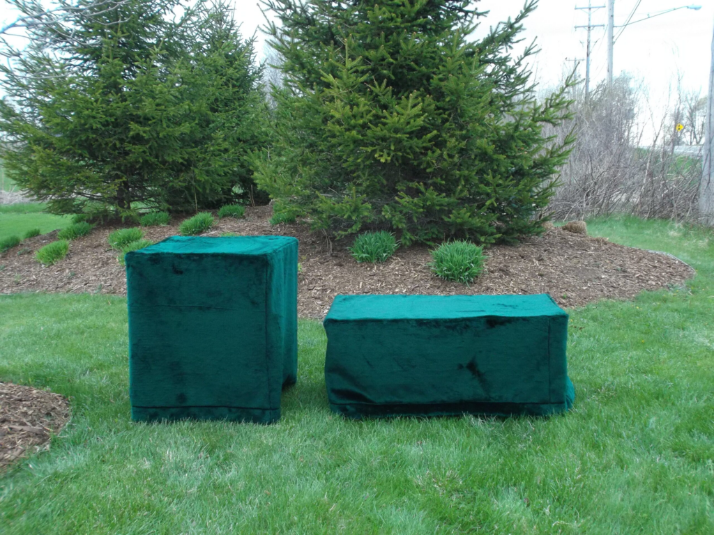Two green, velvet-covered cremation stands rest on the grass, their rectangular forms framed by trees in the background.