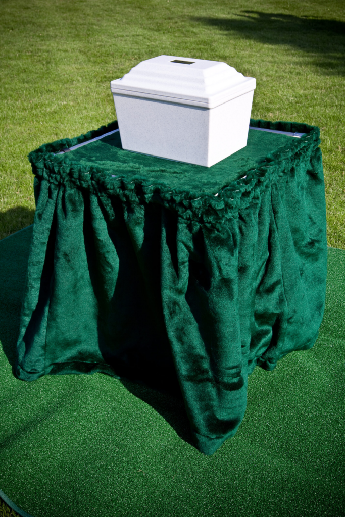 A white urn sits gracefully on a cremation stand, elegantly draped with green velvet cloth, positioned perfectly on the lush grass lawn.