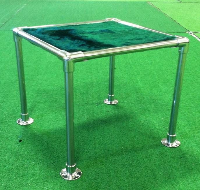 A small metal-framed table, resembling elegant cremation stands, boasts a teal-green top sitting gracefully on a green carpeted floor.