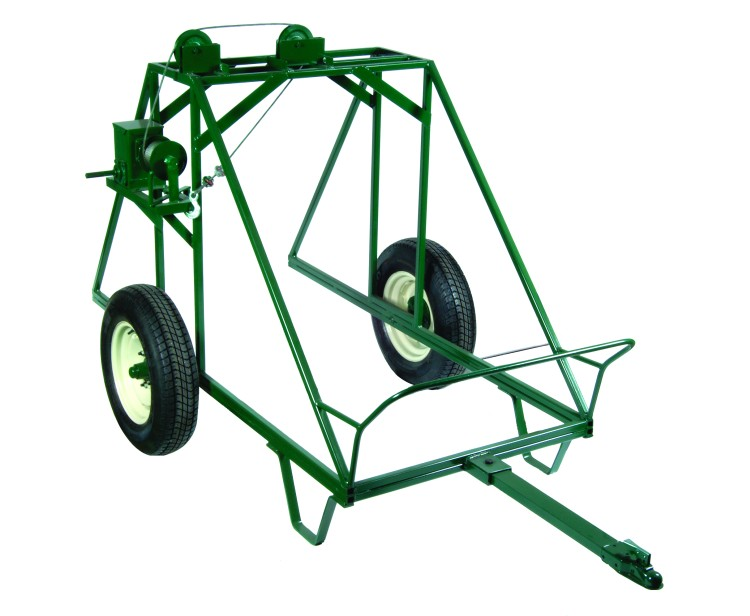 Green metal frame hay bale handler trailer with two black tires, a towing hitch, and winch mechanism, designed for transporting large hay bales.