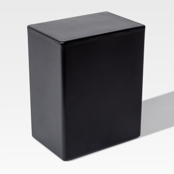 A plain black rectangular box with smooth edges, often used for cremation supplies, is placed on a light surface, casting a shadow to the right.